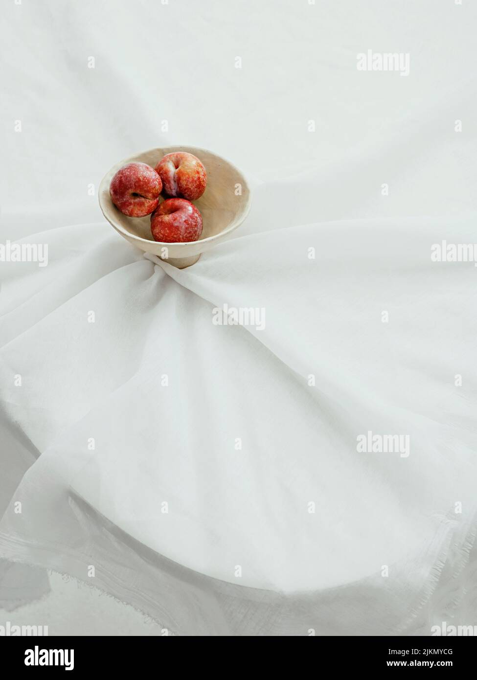 Un colpo estetico verticale di mele in una ciotola bianca su un tavolo con copertura in tessuto bianco Foto Stock