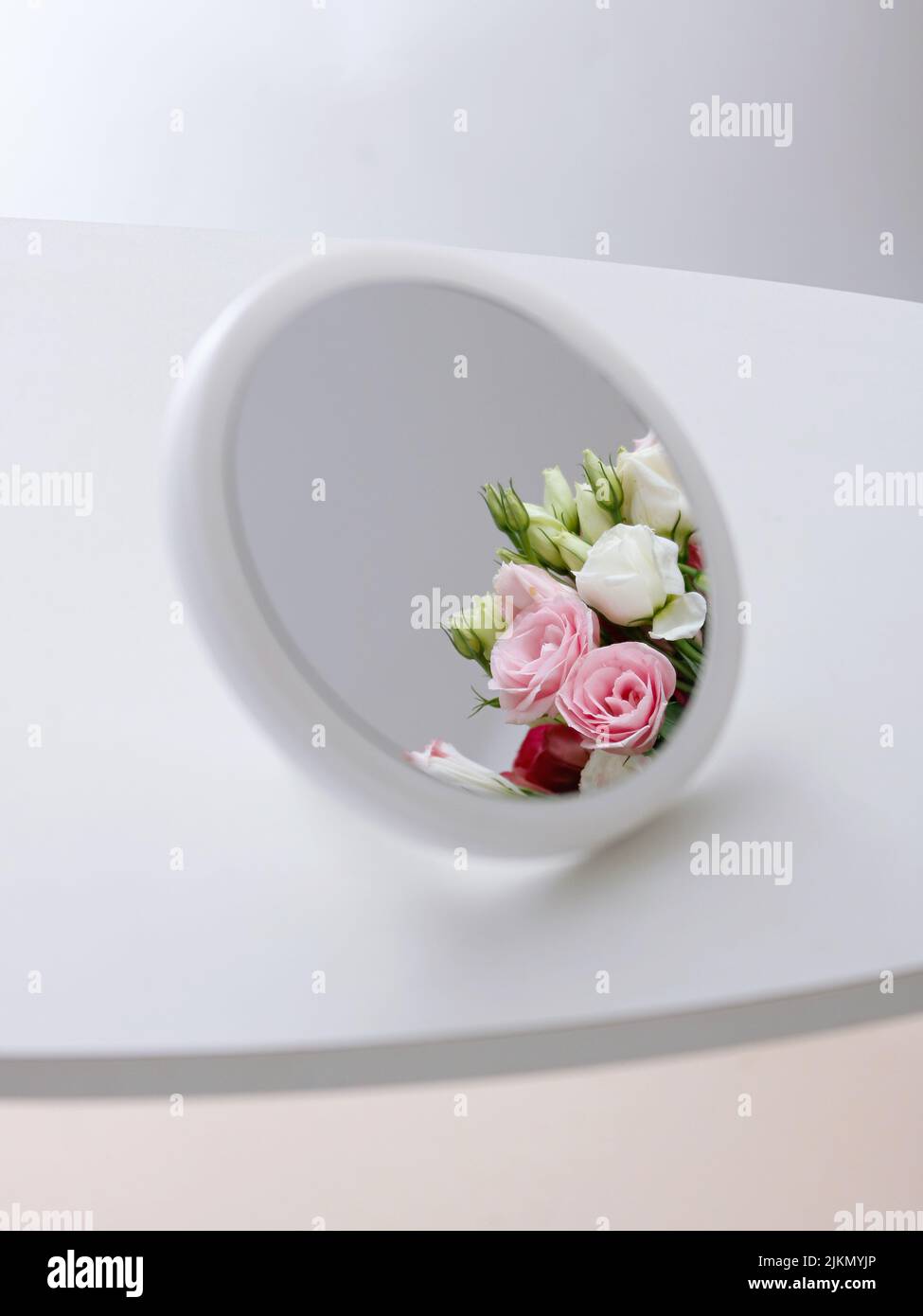 Uno scatto estetico verticale di un bouquet di fiori di rosa visto attraverso un piccolo specchio su una superficie bianca Foto Stock