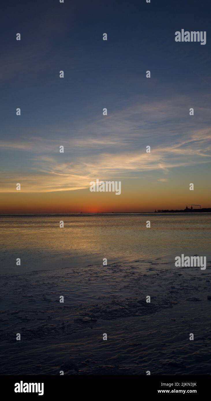 Uno scatto verticale di un tramonto ipnotico sull'orizzonte e sulle onde del mare Foto Stock