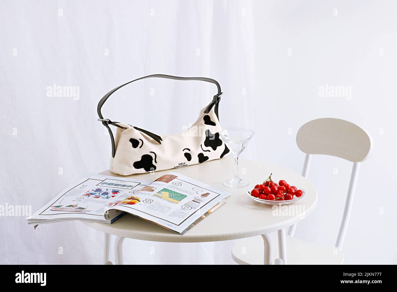 Un giornale, una borsetta e ciliegie rosse su un tavolo su sfondo bianco Foto Stock