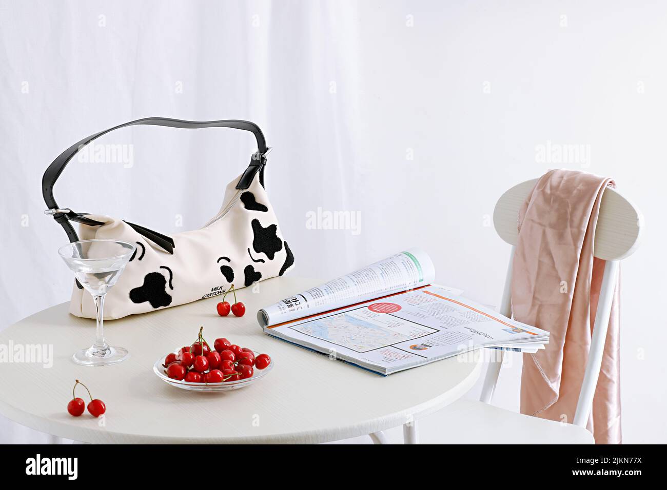 Un giornale, una borsetta e ciliegie rosse su un tavolo su sfondo bianco Foto Stock
