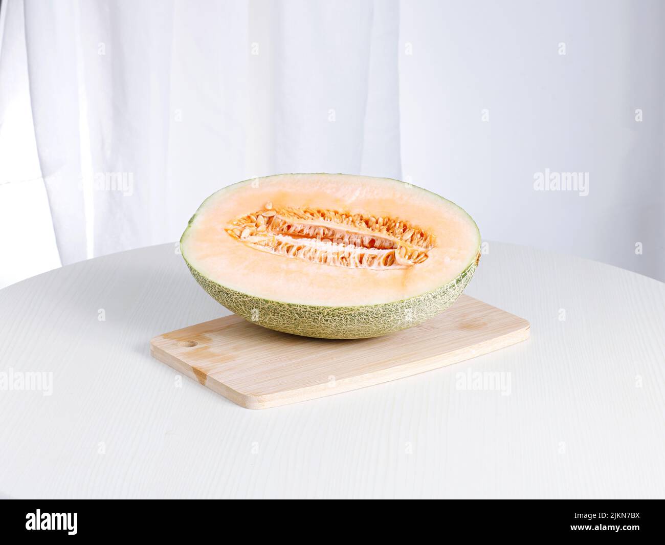 Un melone fresco maturo su un tagliere su un tavolo bianco Foto Stock