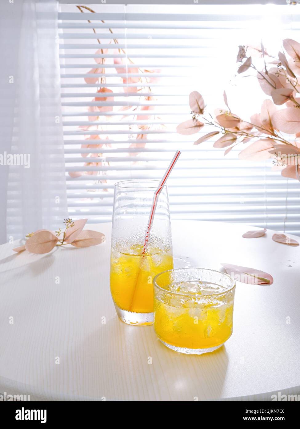 Un colpo verticale di una composizione estetica con succo d'arancia in coppe di vetro con cubetti di ghiaccio su un tavolo Foto Stock