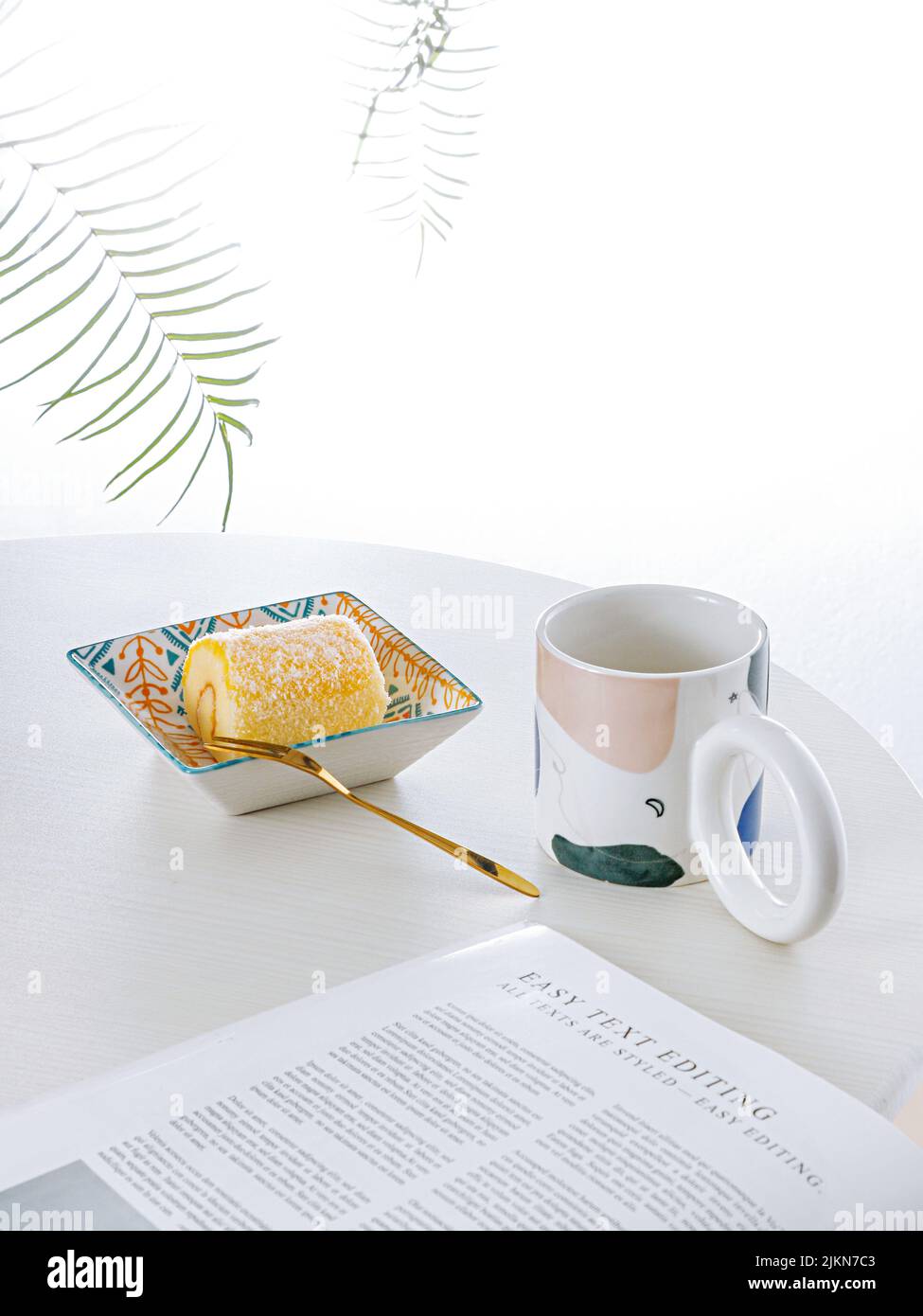 Una foto verticale di allestimento da tavolo con dessert svizzero a rullo e una tazza di tè su sfondo bianco Foto Stock