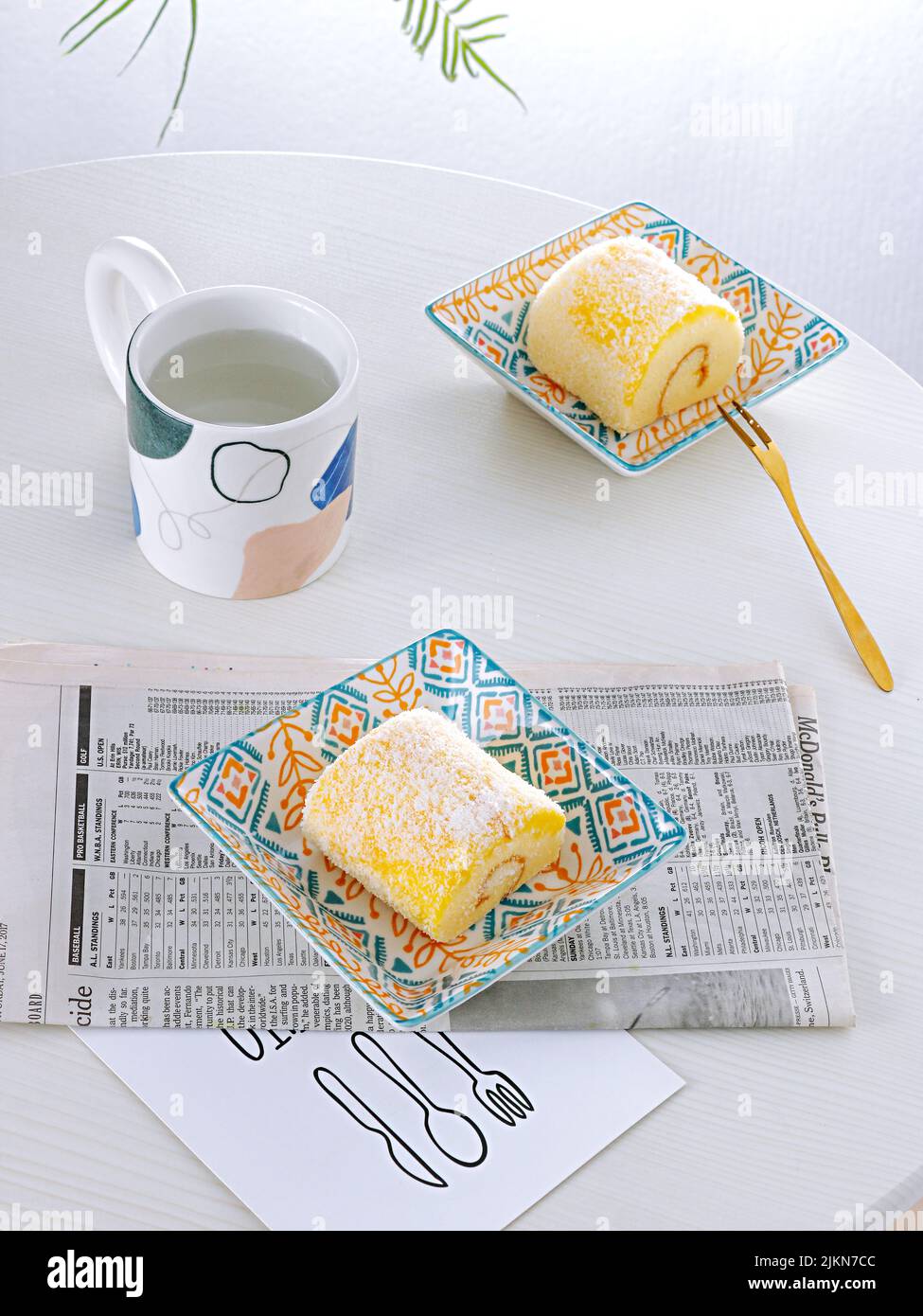 Una foto verticale di allestimento da tavolo con dessert svizzero a rullo e una tazza di tè su sfondo bianco Foto Stock