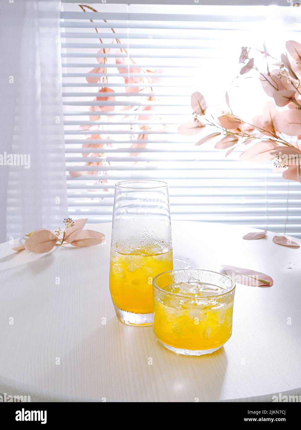 Un colpo verticale di una composizione estetica con succo d'arancia in coppe di vetro con cubetti di ghiaccio su un tavolo Foto Stock