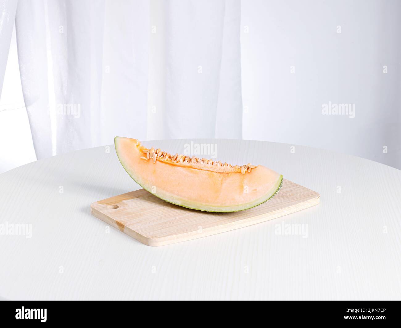 Un melone fresco maturo su un tagliere su un tavolo bianco Foto Stock