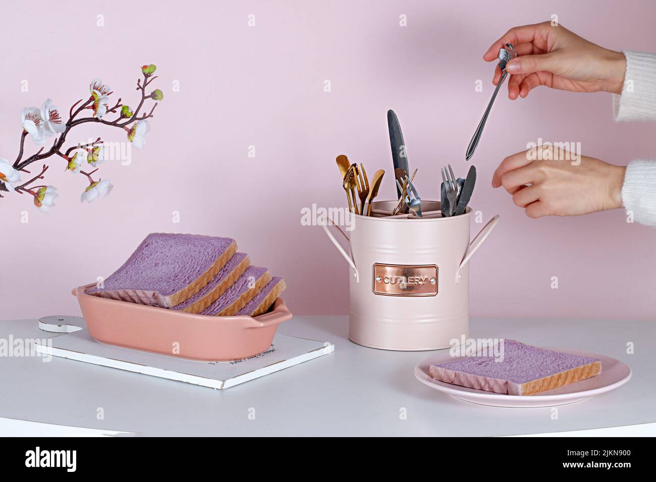 Una persona che allestisce un bel tavolo estetico con pane dolce viola, un set di posate e fiori Foto Stock