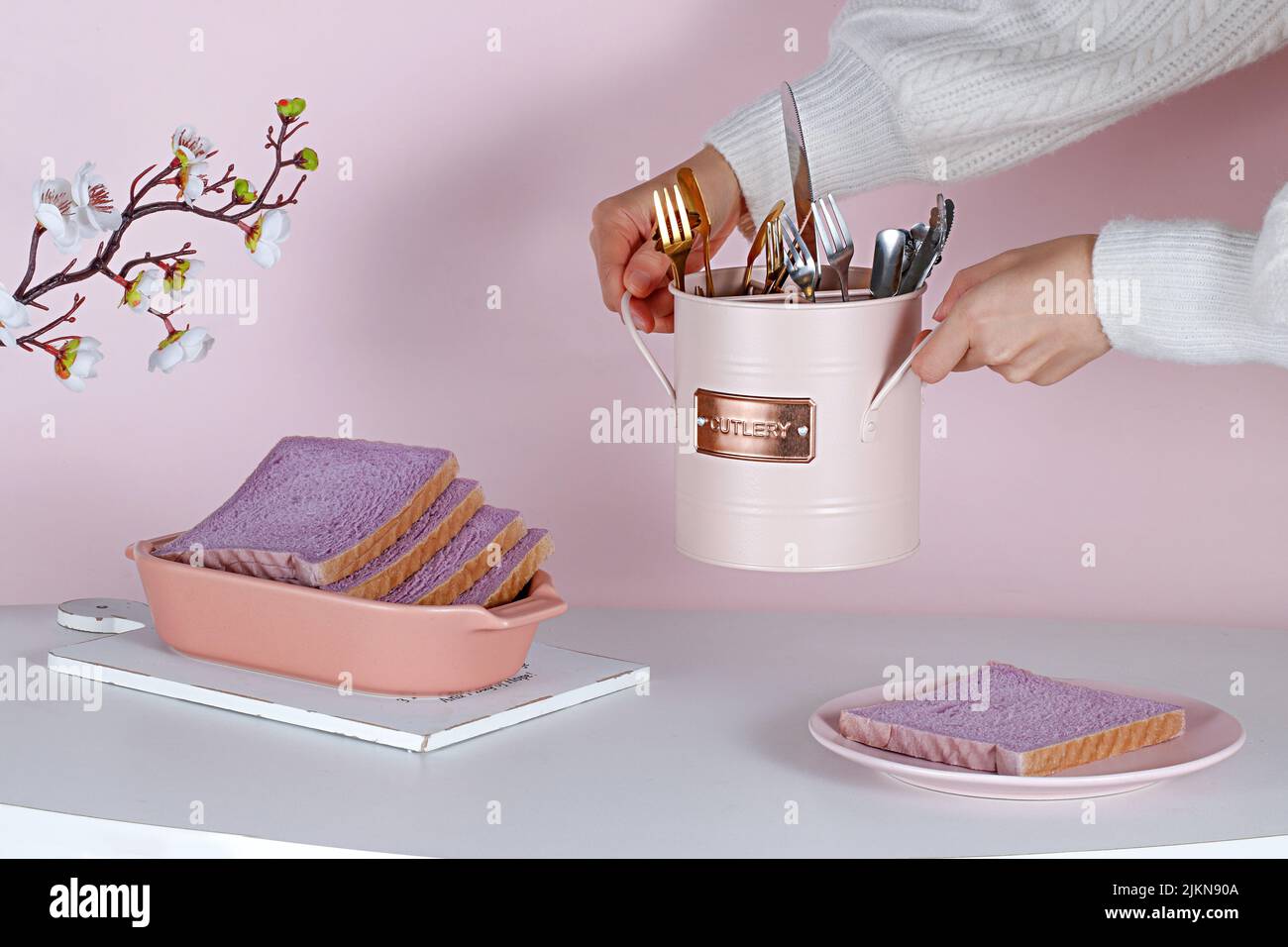 Una persona che allestisce un bel tavolo estetico con pane dolce viola, un set di posate e fiori Foto Stock