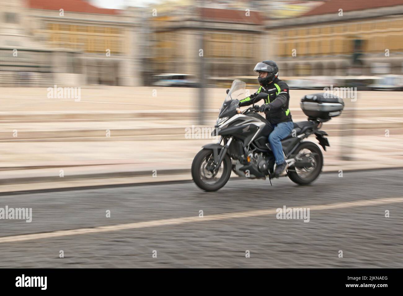 Un uomo che guida una moto ad alta velocità con la vista sfocata dei vecchi edifici di Lisbona Foto Stock