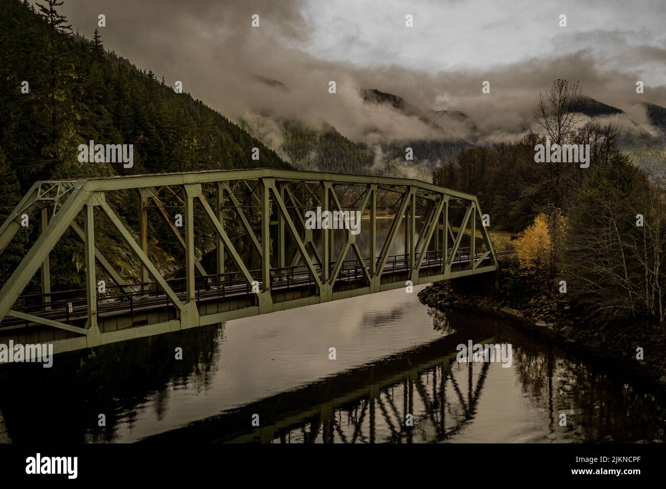 Un bellissimo scatto di un ponte sul fiume con le colline coperte di nebbia sullo sfondo Foto Stock