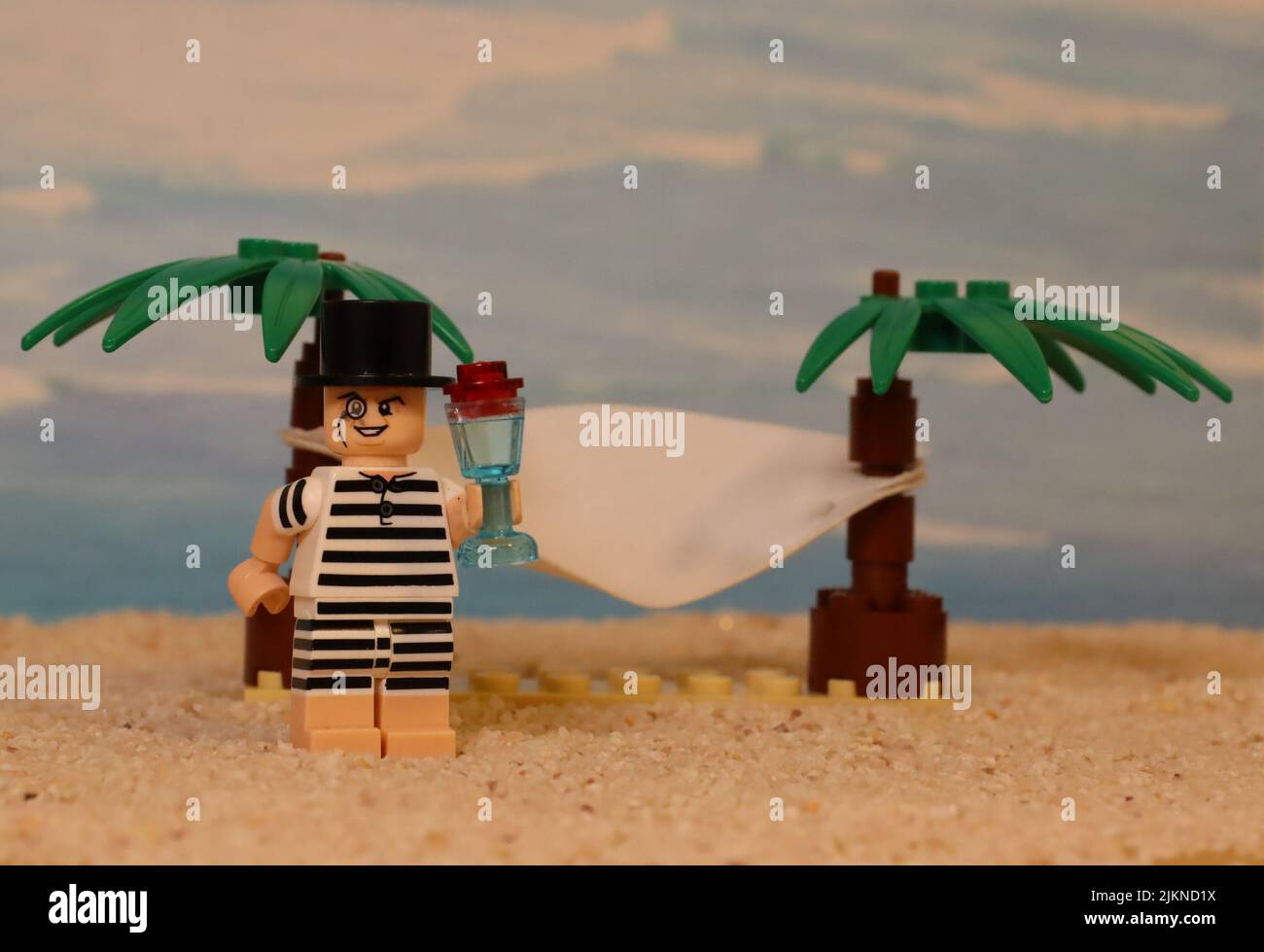 Il personaggio giocattolo Lego maschio con un bicchiere da cocktail su uno sfondo di spiaggia sabbiosa con palme da lego Foto Stock