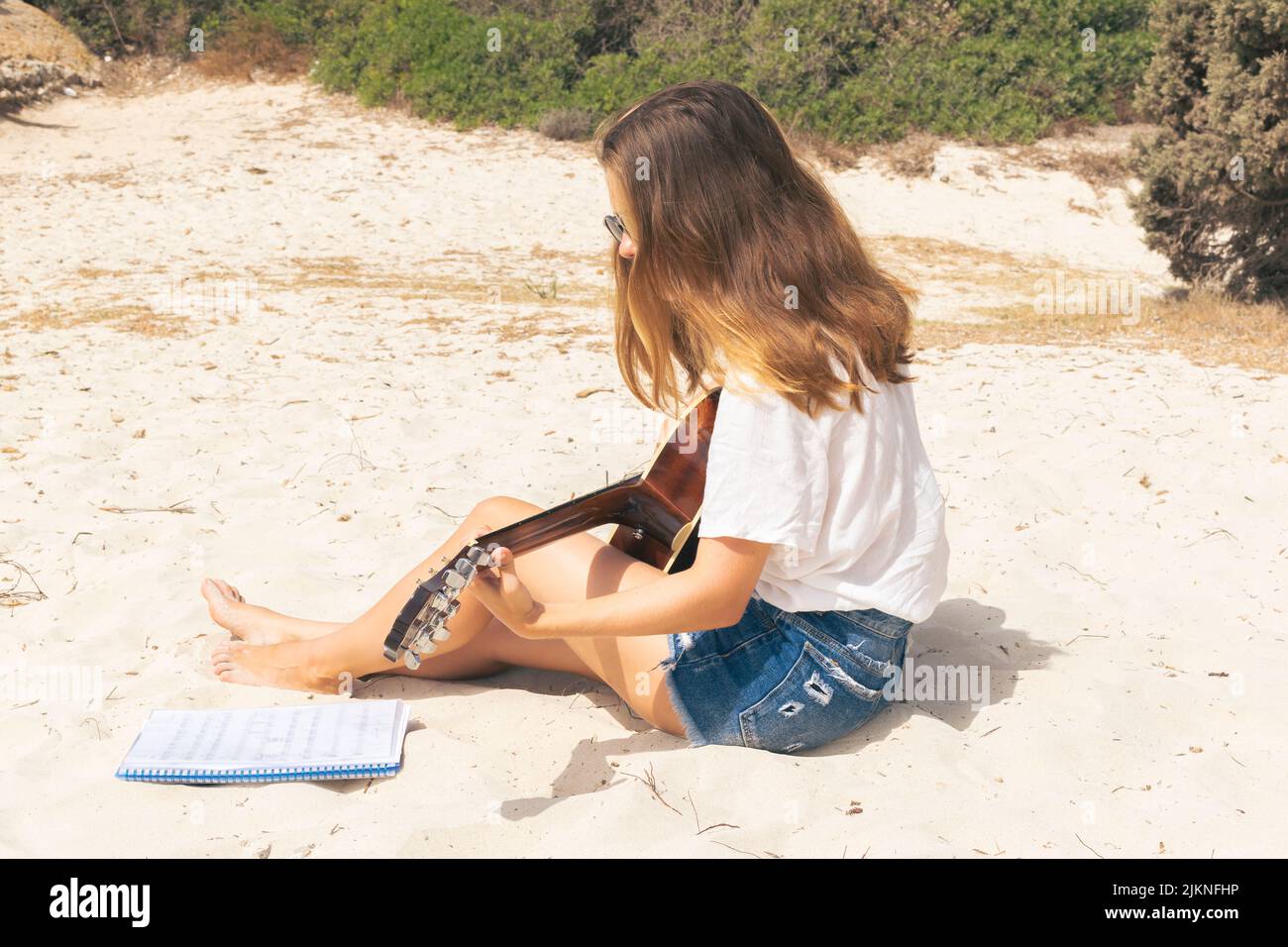 Giovane donna caucasica legge la partitura musicale per suonare una canzone sulla spiaggia. Foto Stock