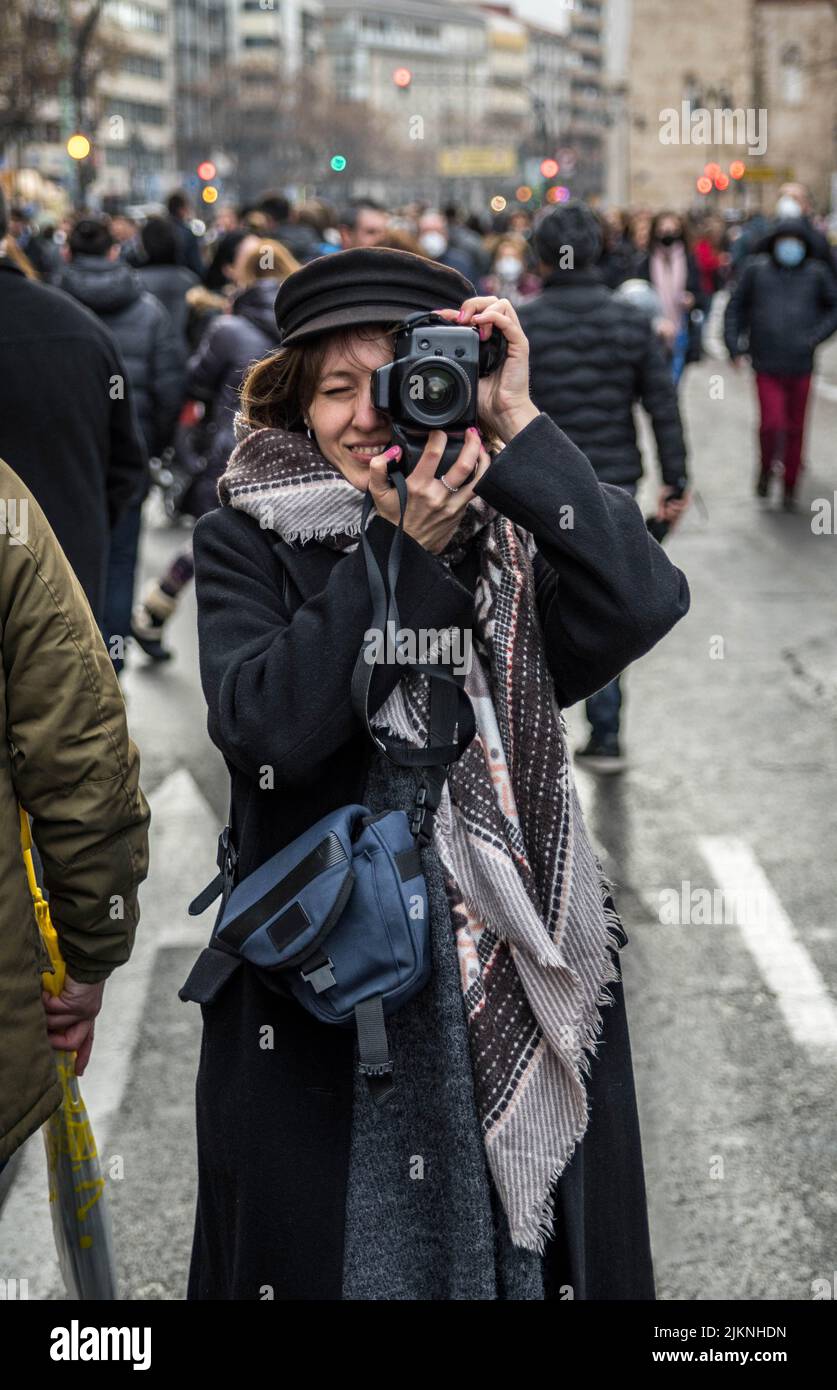 Foto di ragazza divertirsi scattare foto con una fotocamera DSLR in una strada affollata con cappotto nero e Beret. (Foto verticale) Foto Stock