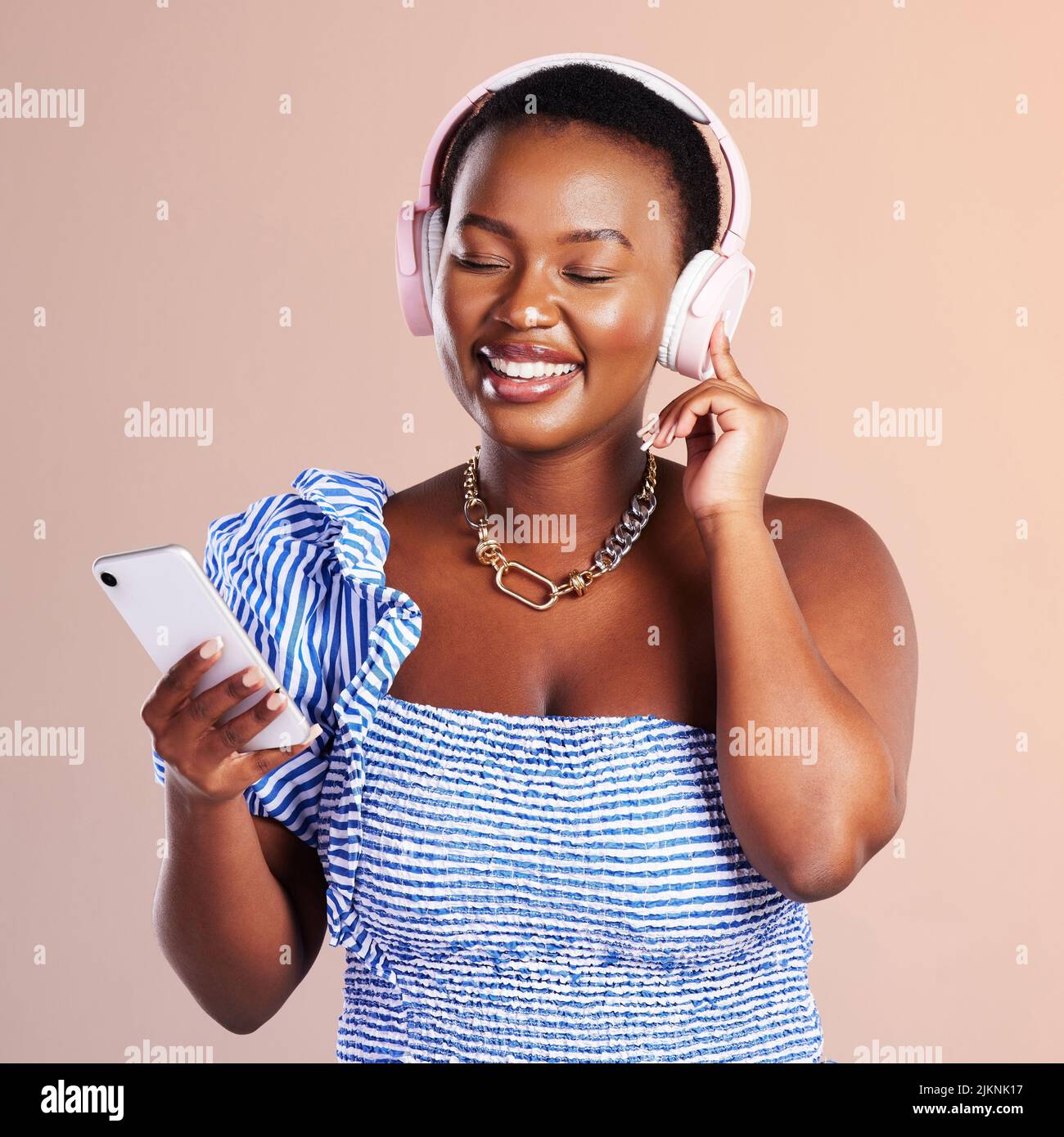 La creatività fiorisce nella solitudine. Studio girato di una giovane donna utilizzando uno smartphone e le cuffie su sfondo rosa. Foto Stock