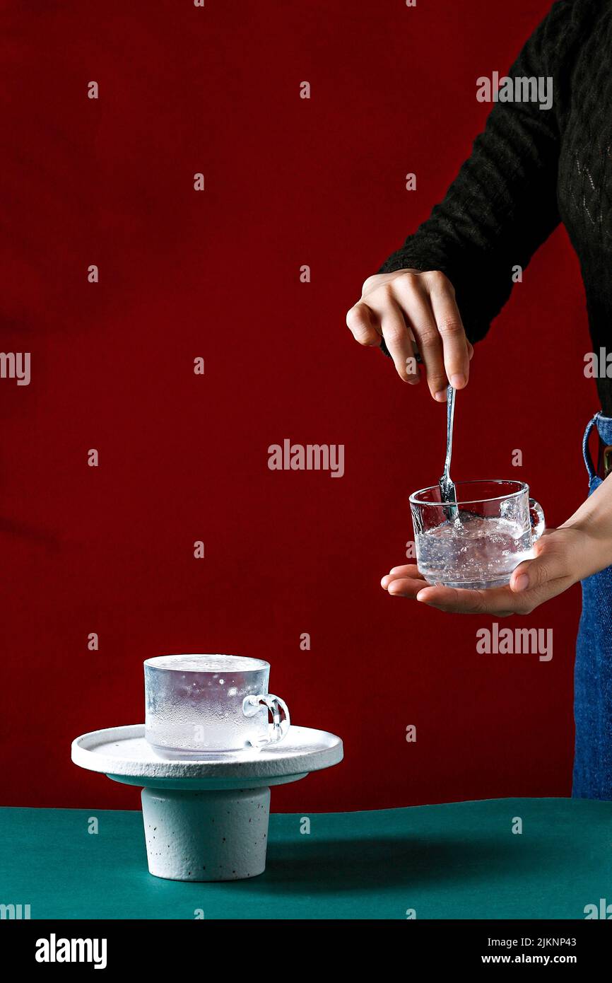 Una ragazza che tiene una tazza con liquido freddo e stipare con un cucchiaio vicino al muro rosso con spazio copia Foto Stock