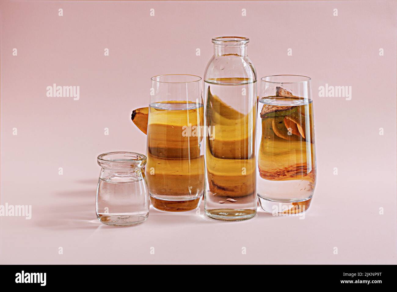 Una bottiglia d'acqua trasparente e tre bicchieri con dietro le banane su sfondo rosa Foto Stock