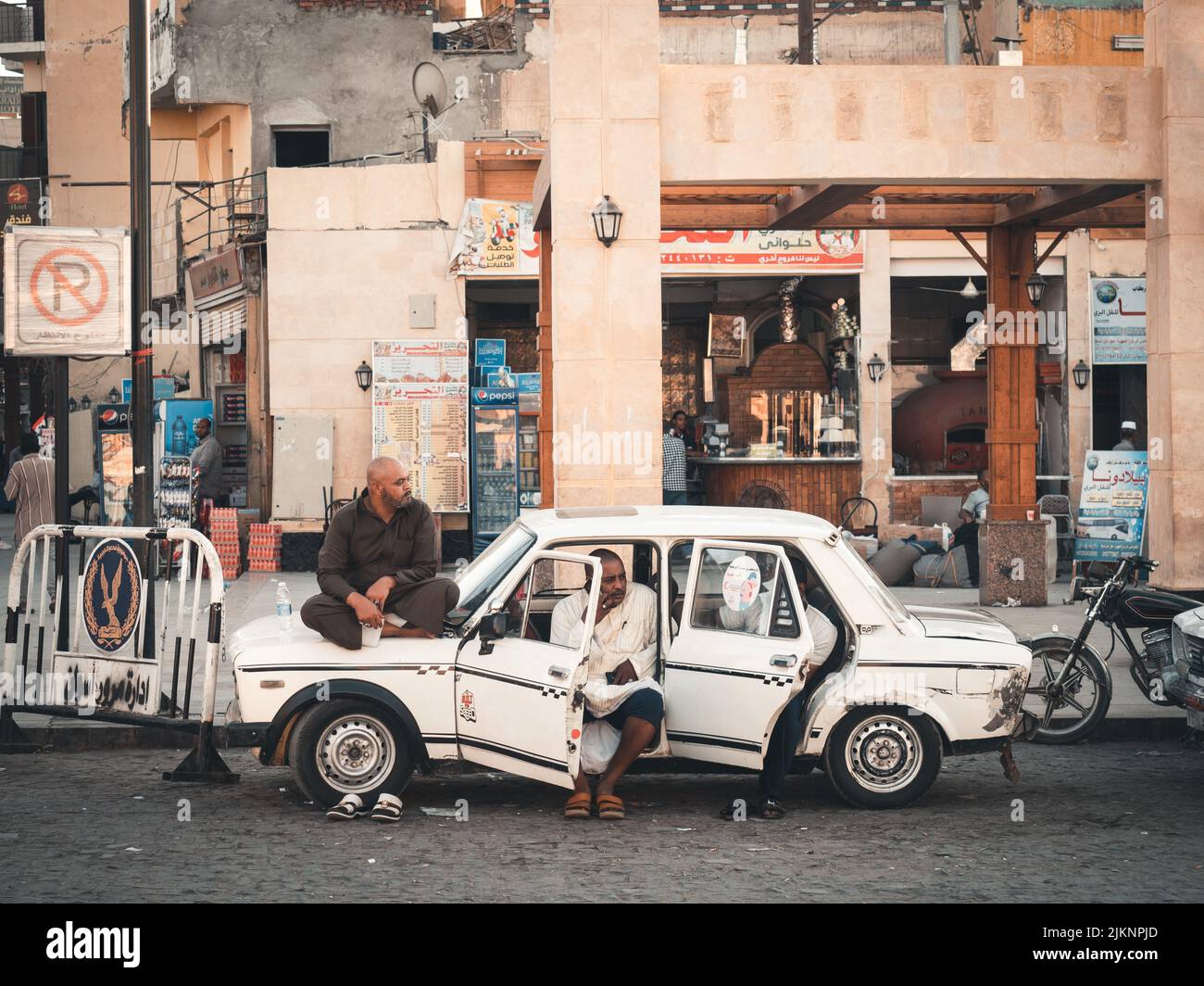Una foto di strada di due ragazzi locali seduti in un taxi d'epoca bianco ad Assuan con un vecchio edificio sullo sfondo Foto Stock
