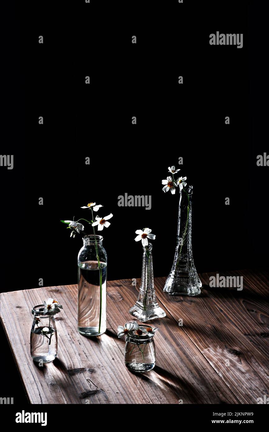 Un primo piano verticale di vasi di fiori trasparenti su un tavolo di legno su sfondo scuro Foto Stock