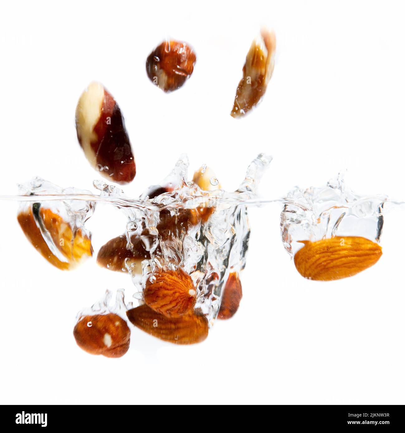 Un primo piano di un assortimento di noci candite che cadono in acqua su sfondo bianco Foto Stock