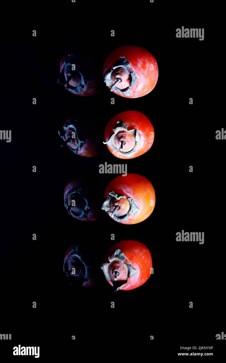 Un colpo verticale di Persimmons maturo isolato su sfondo nero Foto Stock