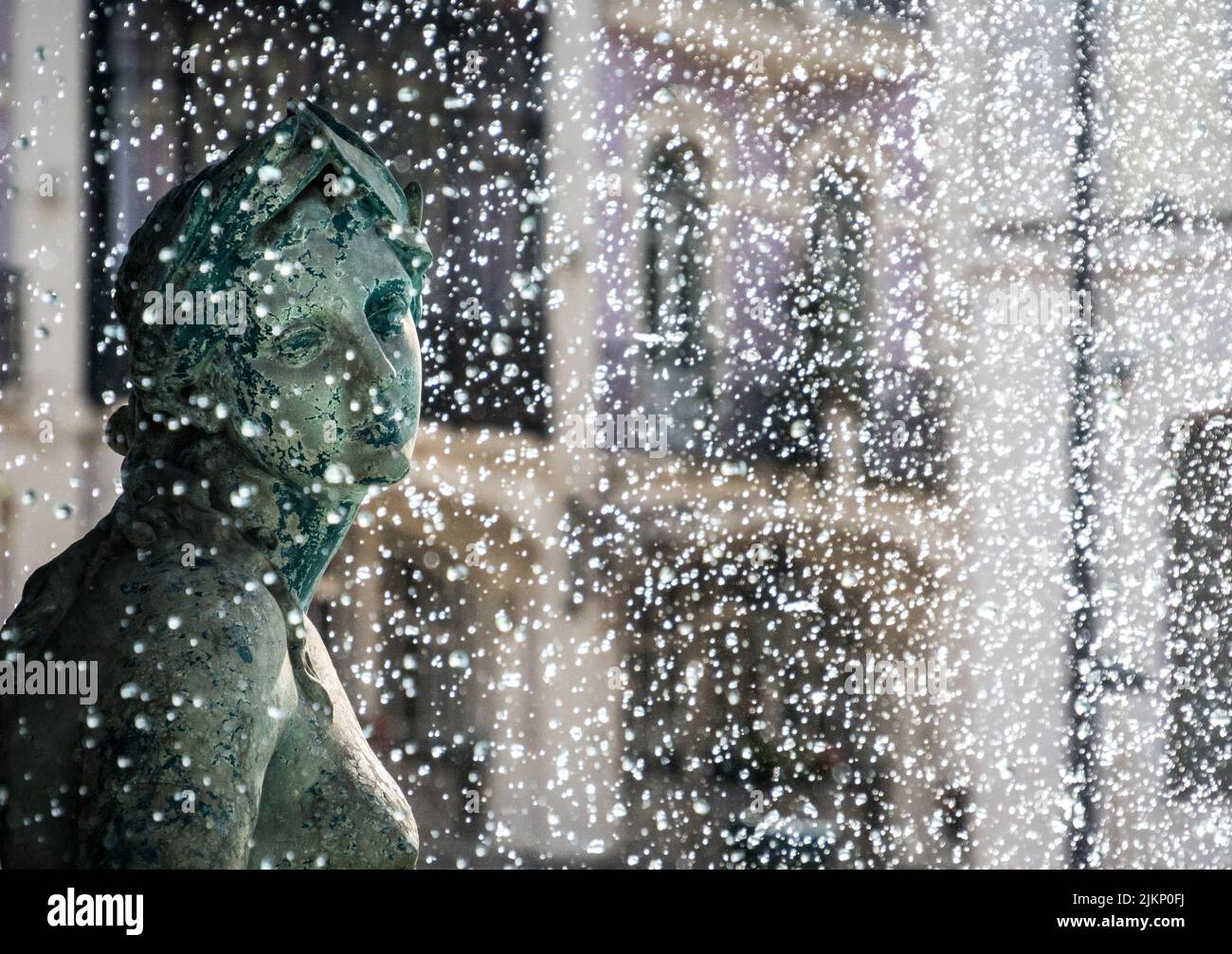 Una dozzina di gocce d'acqua che spruzzano sulla statua femminile con un volto premuroso Foto Stock