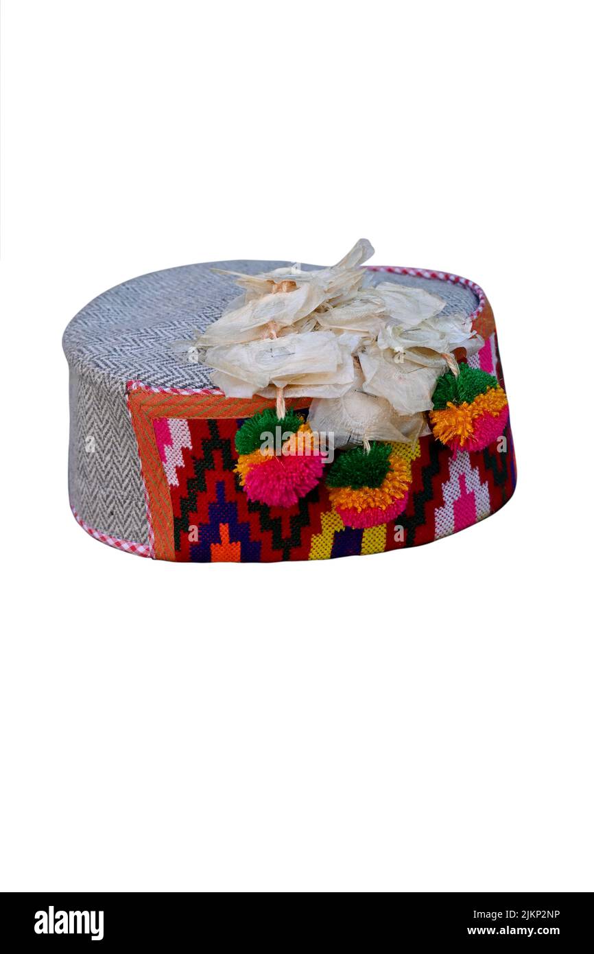 primo piano la colorata mano fatto himachali indiano tradizionale cappello con appendere fiori bianchi isolato su sfondo bianco. Foto Stock