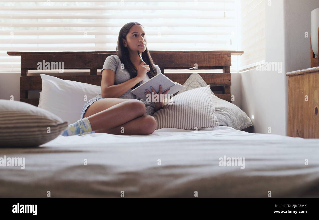 Impostare obiettivi e intenzioni. Una giovane donna seduta a letto mentre scrive nel suo diario a casa. Foto Stock