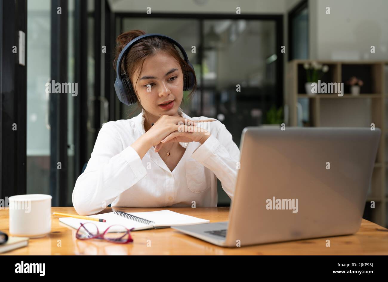 Educazione online, e-learning. Giovane donna che studia da remoto, usando un notebook, ascoltando una conferenza online, prendendo appunti mentre si siede a casa, sorride Foto Stock