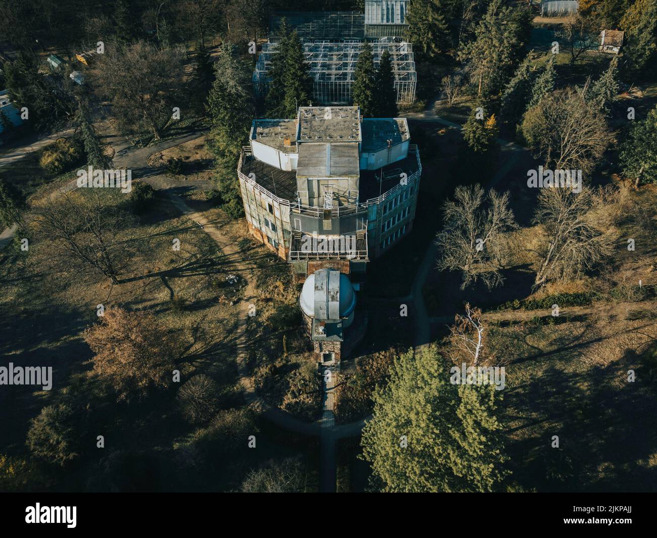 Un'immagine ad alto angolo di un edificio postmoderno abbandonato in un parco verde intorno agli alberi al sole Foto Stock