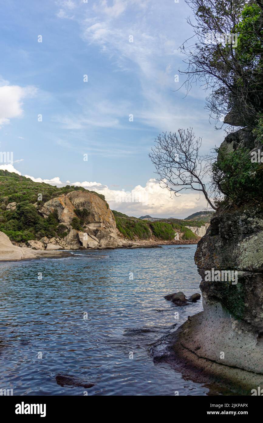 Uno scatto verticale di un fiume fiancheggiato da scogliere rocciose sotto un cielo azzurro nuvoloso in Sardegna Foto Stock