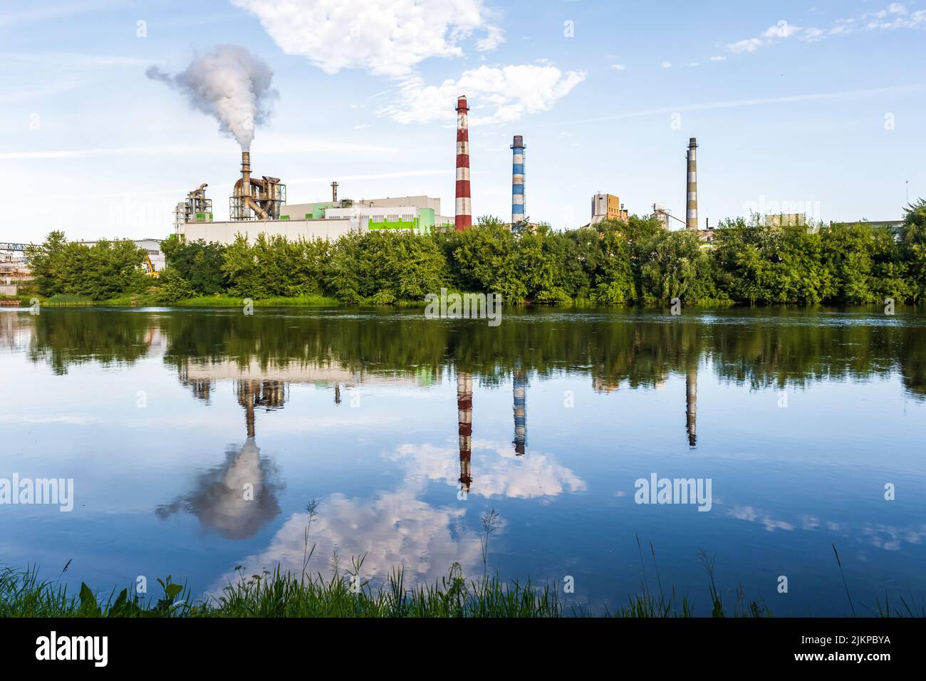 pipe di impresa di lavorazione del legno pianta segheria con bella riflessione in acqua blu del fiume. Concetto di inquinamento atmosferico. Ambienti industriali del paesaggio Foto Stock