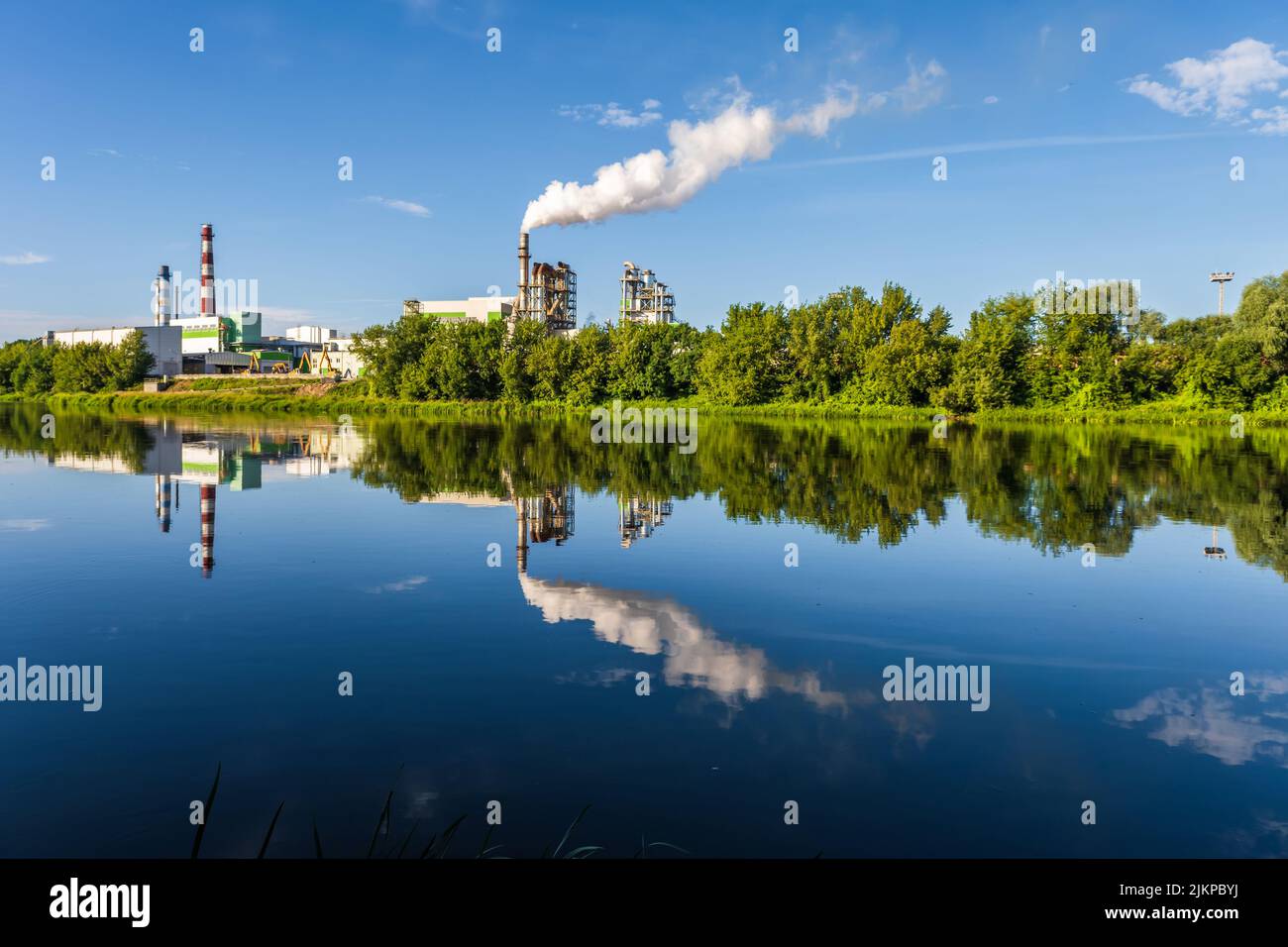 pipe di impresa di lavorazione del legno pianta segheria con bella riflessione in acqua blu del fiume. Concetto di inquinamento atmosferico. Ambienti industriali del paesaggio Foto Stock