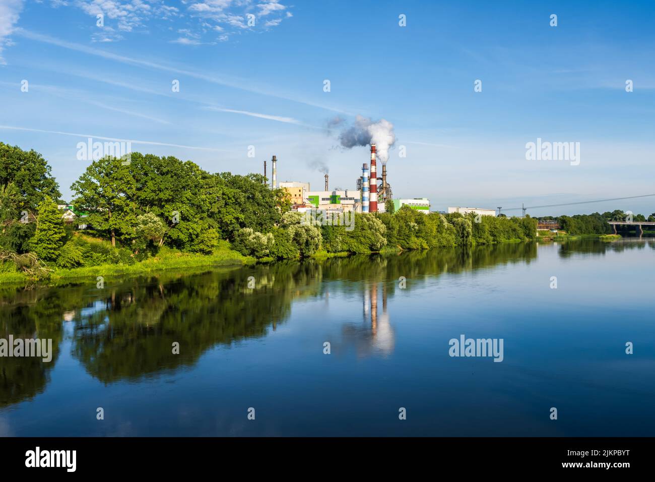 pipe di impresa di lavorazione del legno pianta segheria con bella riflessione in acqua blu del fiume. Concetto di inquinamento atmosferico. Ambienti industriali del paesaggio Foto Stock