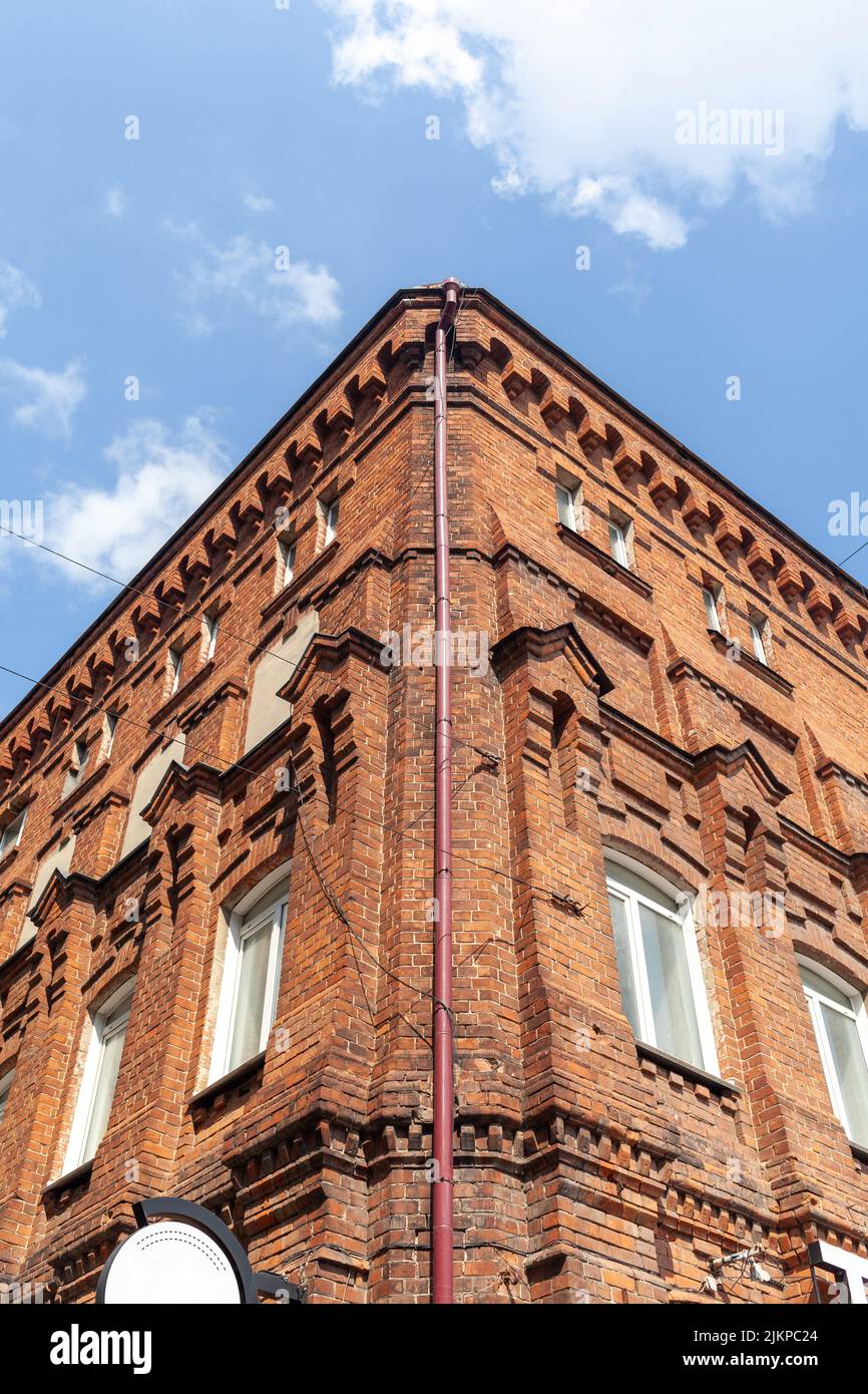 Un vecchio e grande edificio in mattoni con un cartello bianco per il nome di un caffè o di un negozio. Edificio in mattoni nel centro della città ma contro il cielo blu. Foto Stock