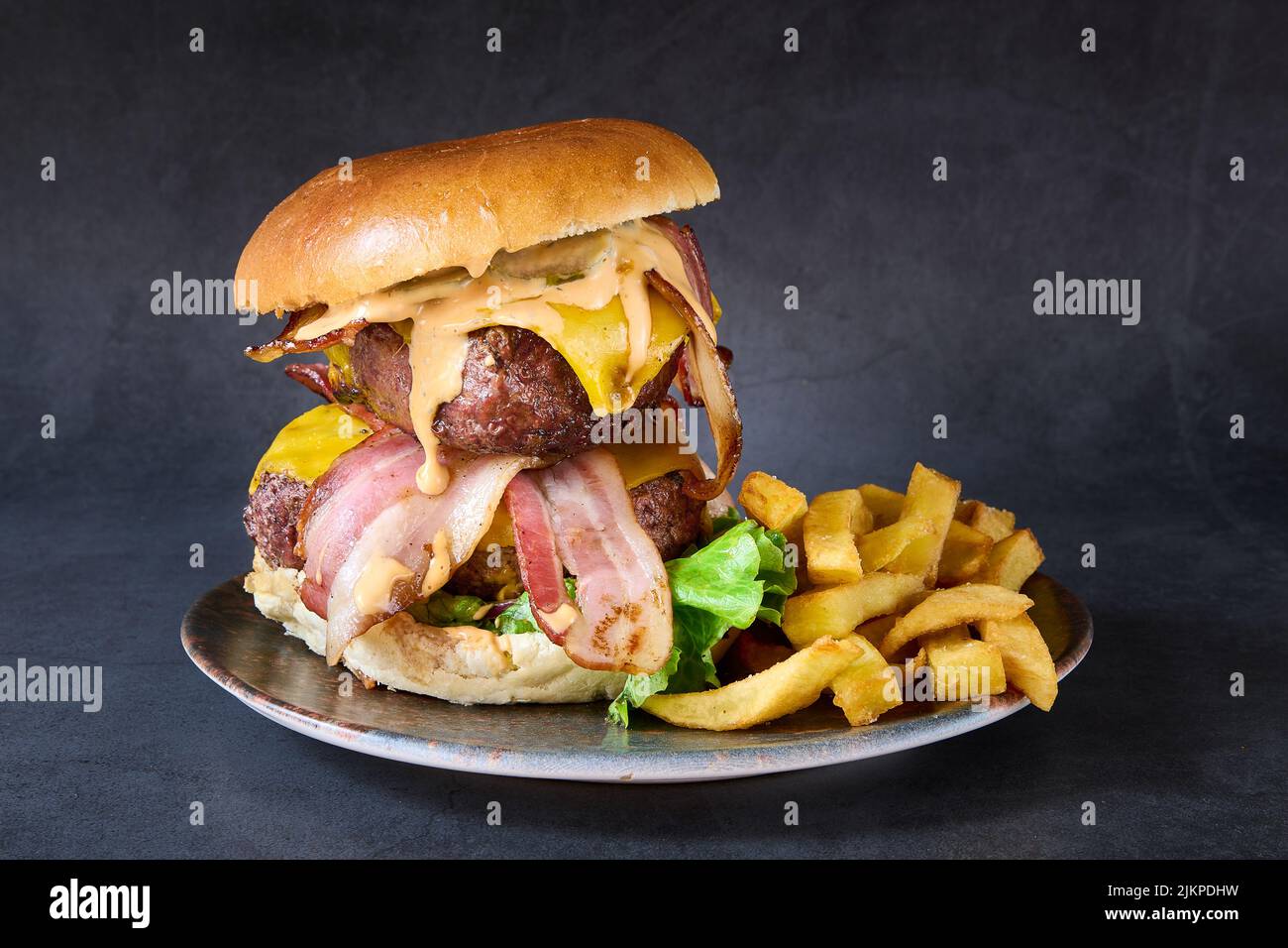 Un primo piano di hamburger bavarese con doppio manzo e patatine fritte sul lato in un piatto. Foto Stock