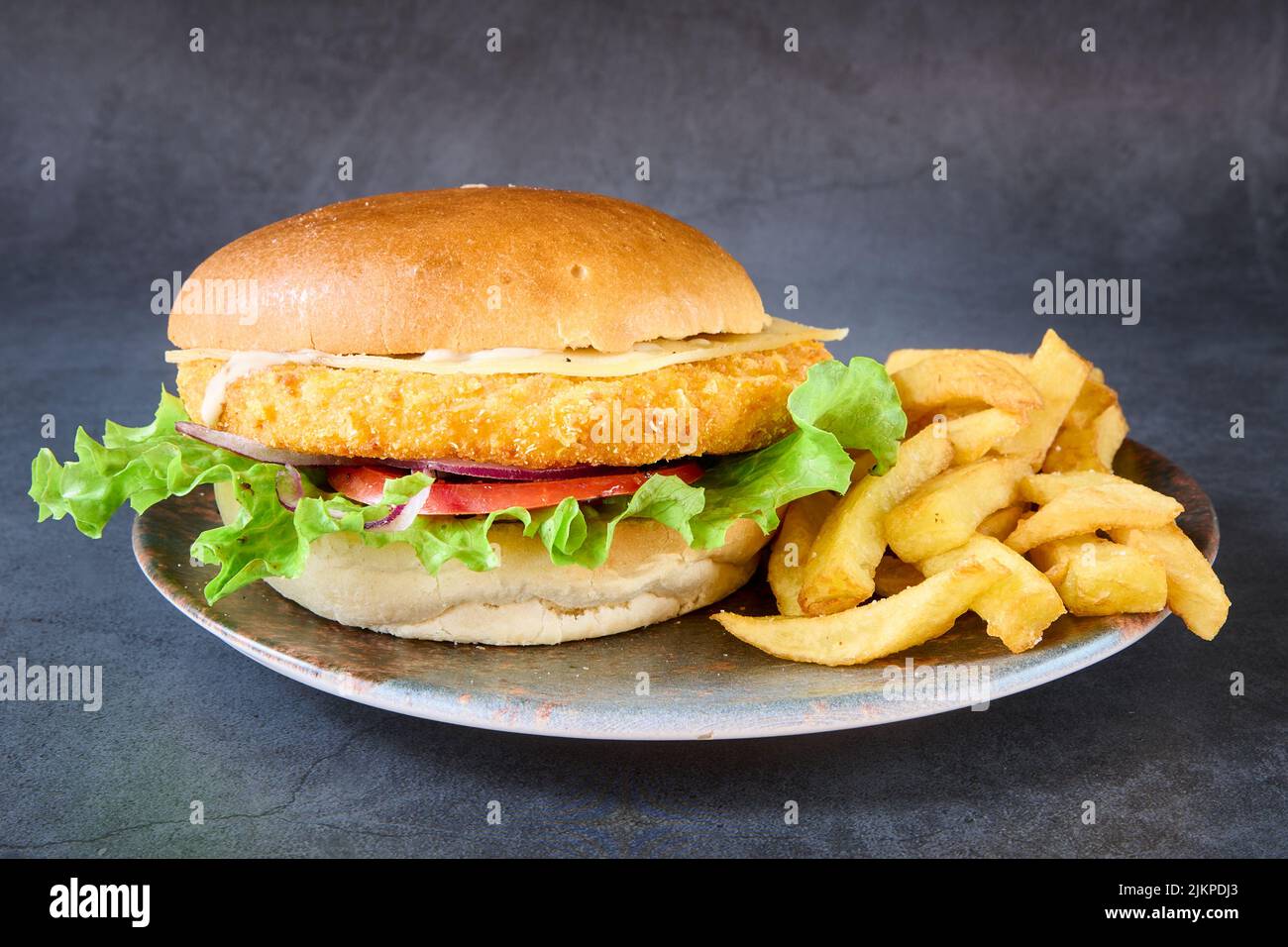 Un primo piano di un hamburger di pollo con patatine fritte su un piatto. Foto Stock