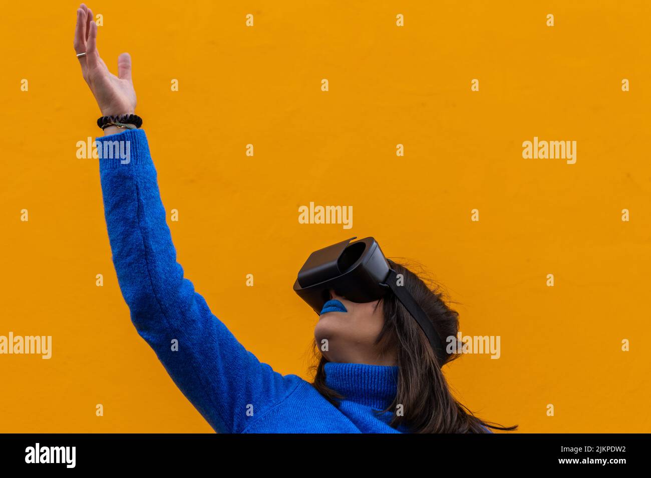 Ritratto isolato di una donna con abiti blu indossando occhiali vr e toccando qualcosa di invisibile in realtà virtuale. Sfondo giallo. Foto Stock