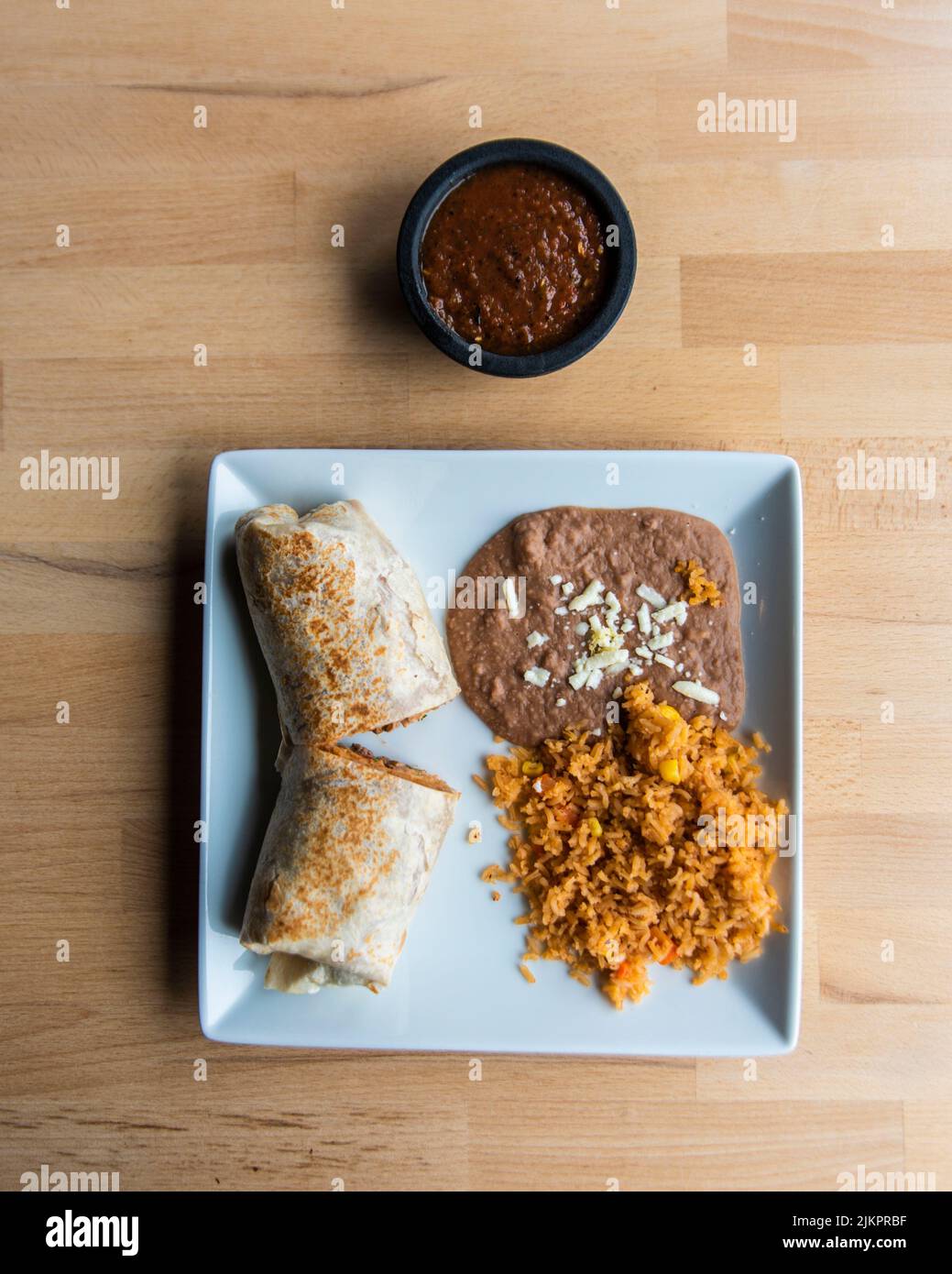 Una vista dall'alto di un piatto con un burrito messicano con riso e fagioli e salsa sul lato Foto Stock