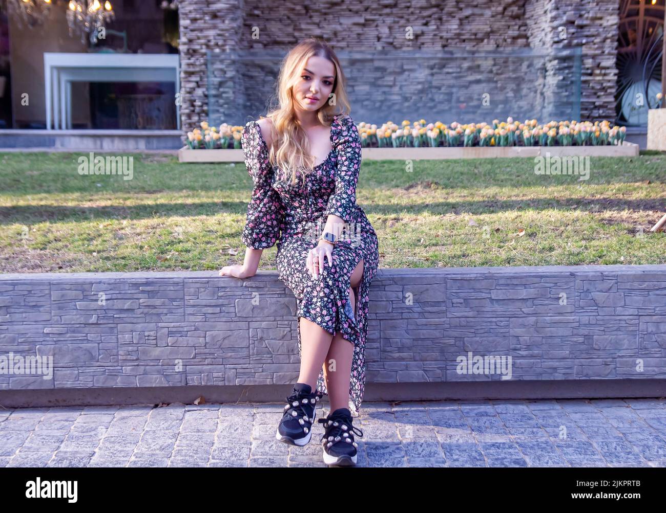 Una bella giovane donna caucasica in un abito floreale seduto su un marciapiede Foto Stock