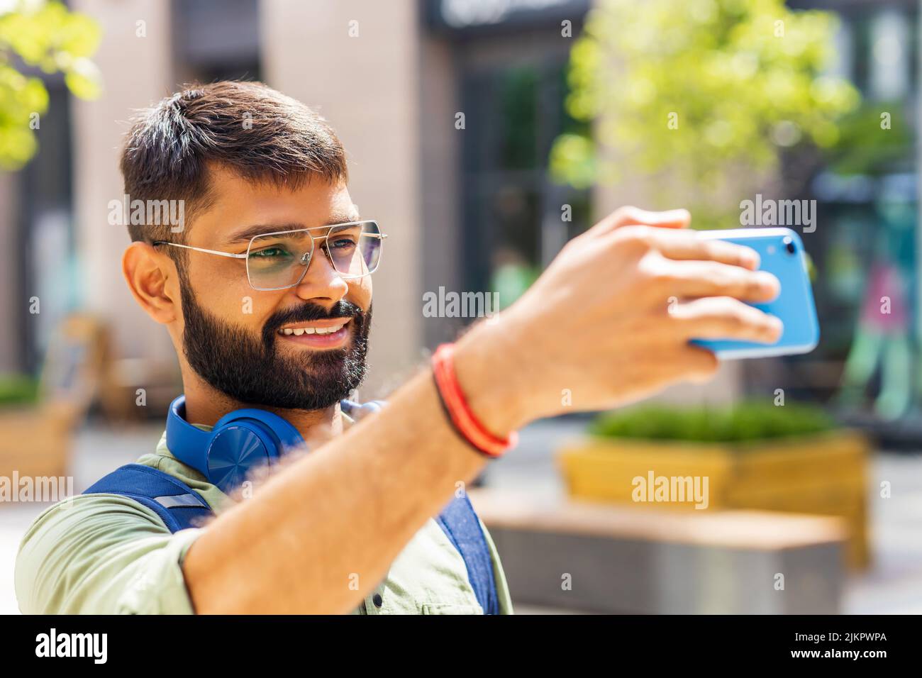 studente indiano con cuffia blu e zaino che scatta foto selfie sullo smartphone nelle giornate di sole Foto Stock