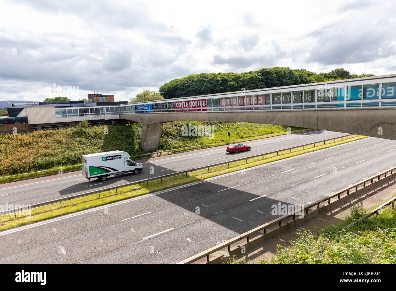 Autostrada M6 presso la stazione di servizio di Lancaster con ponte pedonale sull'autostrada, Lancashire, Inghilterra, Regno Unito Foto Stock