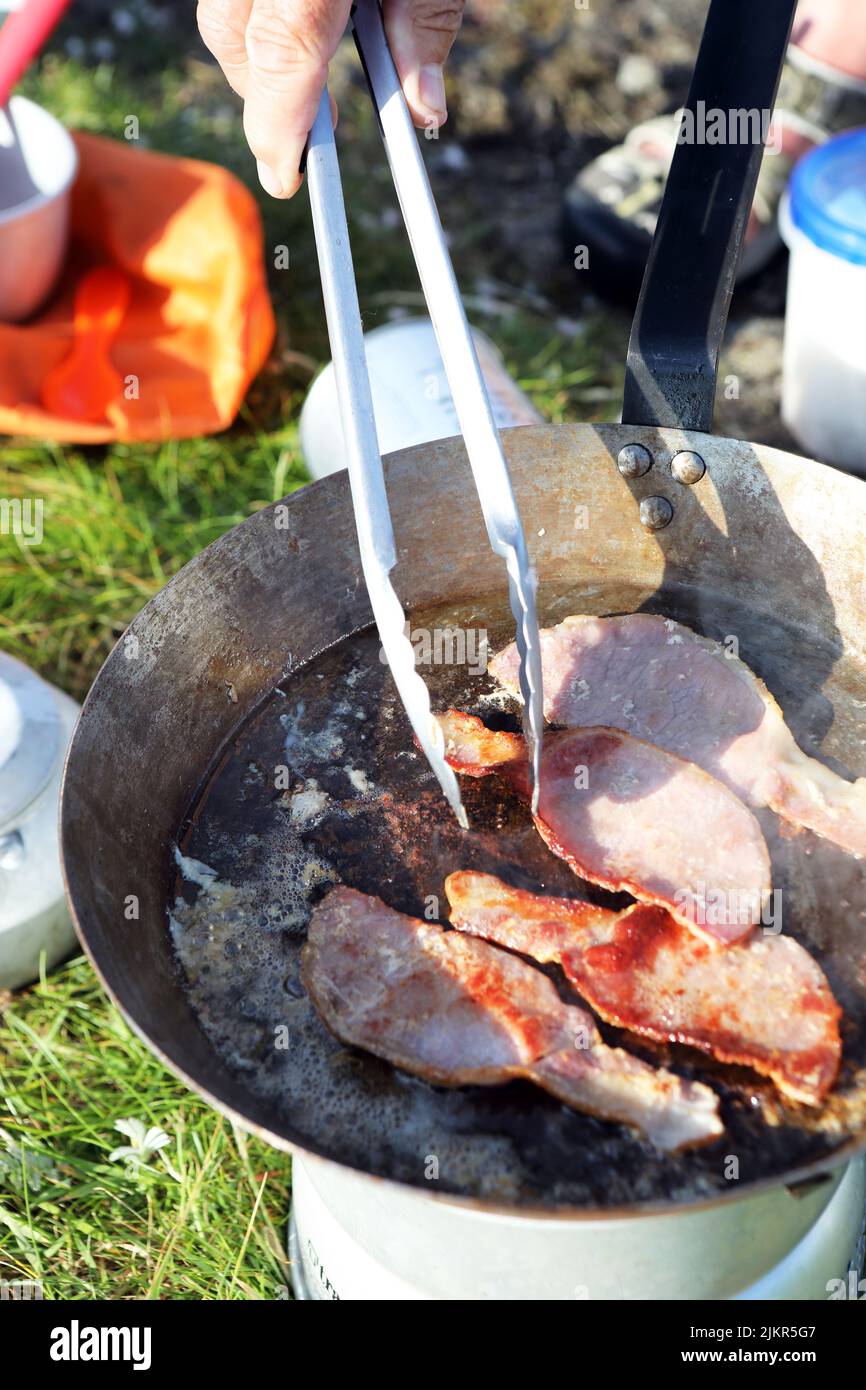 Frittura di bacon su una stufa mentre campeggio selvaggio in Scozia Foto Stock