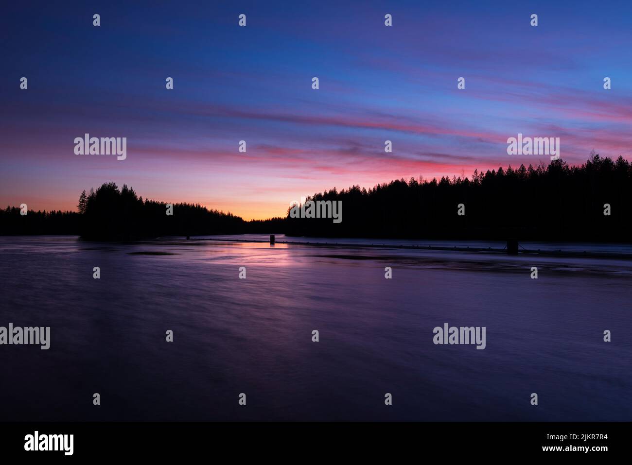 Fiume Pielisjoki che scorre attraverso il paesaggio forestale invernale al crepuscolo. Cielo crepuscolo colorato e i suoi riflessi nell'acqua. Finlandia. Foto Stock