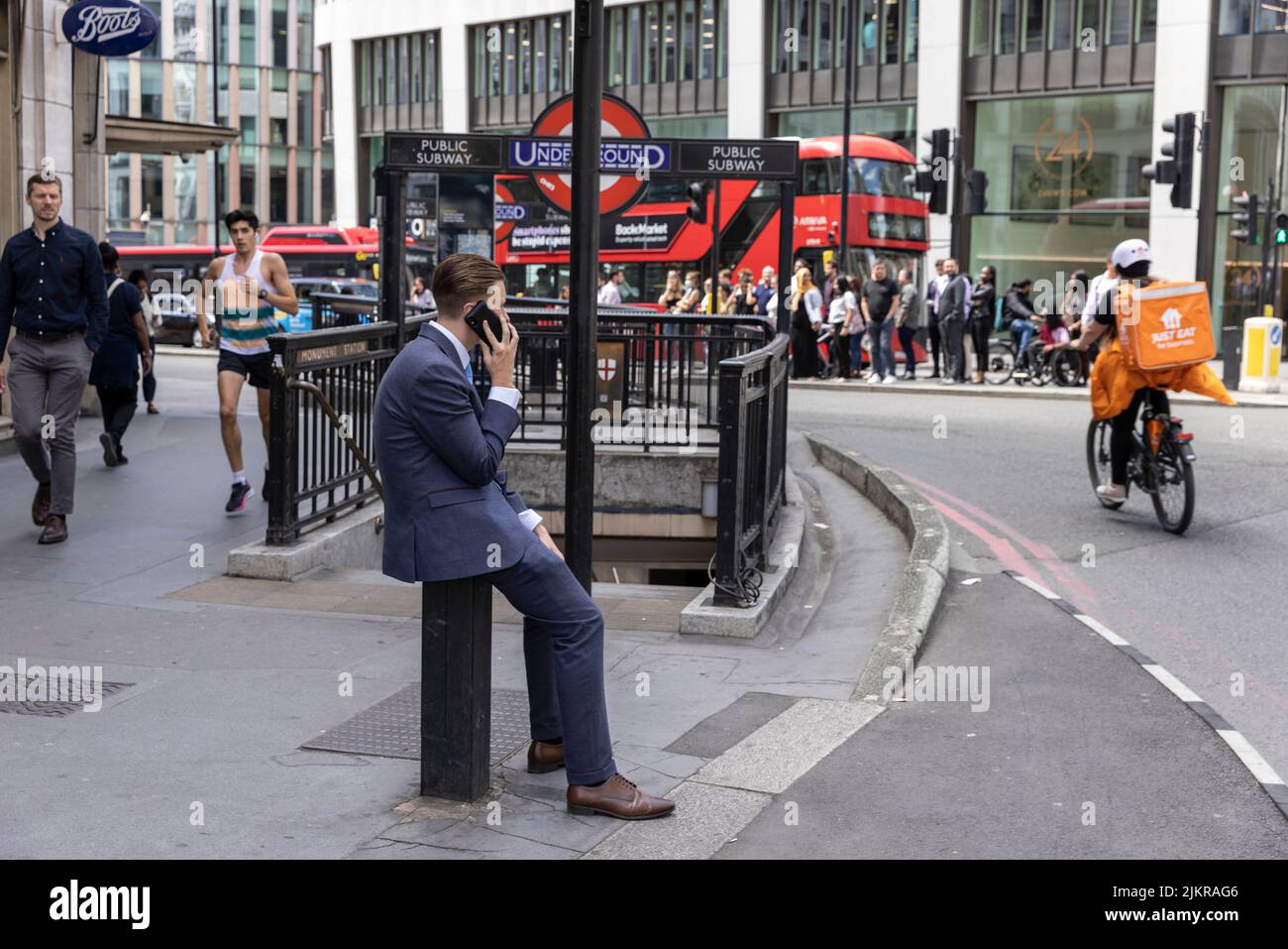 Un giovane cittadino seduto su un pilone metallico mentre parla sul suo cellulare a London Bridge, City of London, England, United Kingdom Foto Stock