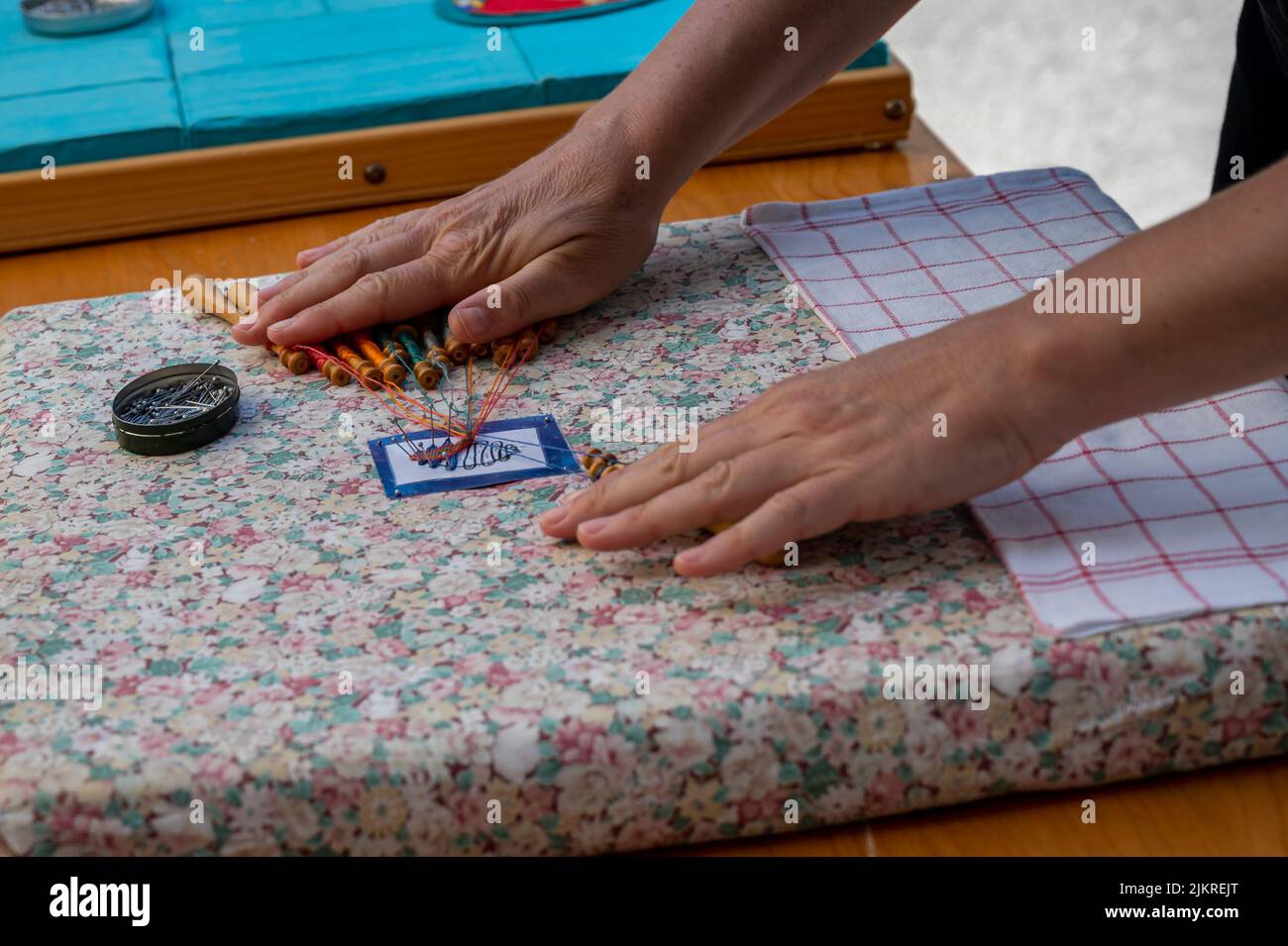 Mani di donna che fanno merletto di bobina. Fili colorati di pizzo. Abilità e creatività. Foto Stock