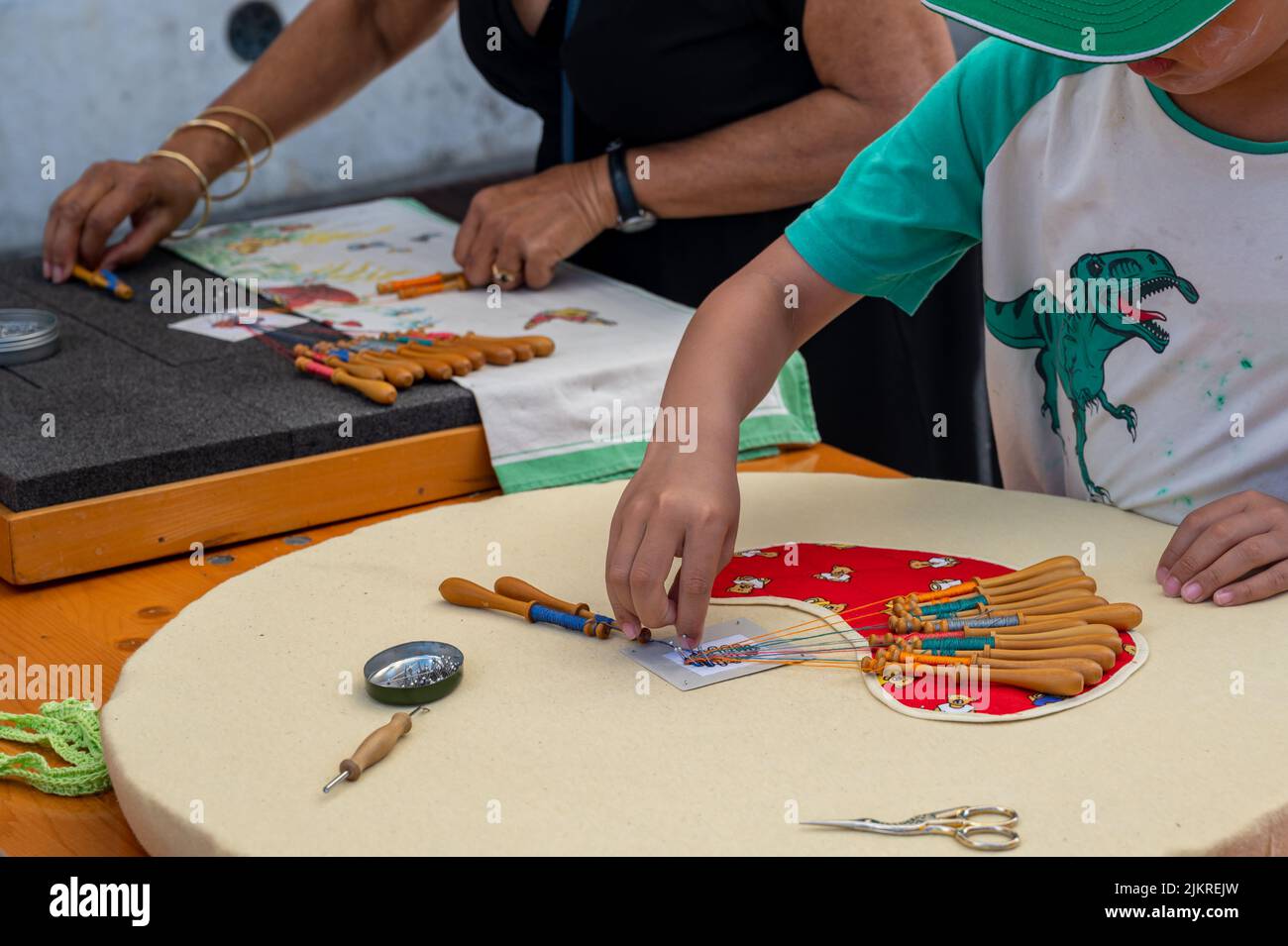 Mani di bambino e adulto che fanno merletto della bobina. Fili colorati di pizzo. Abilità e creatività. Foto Stock