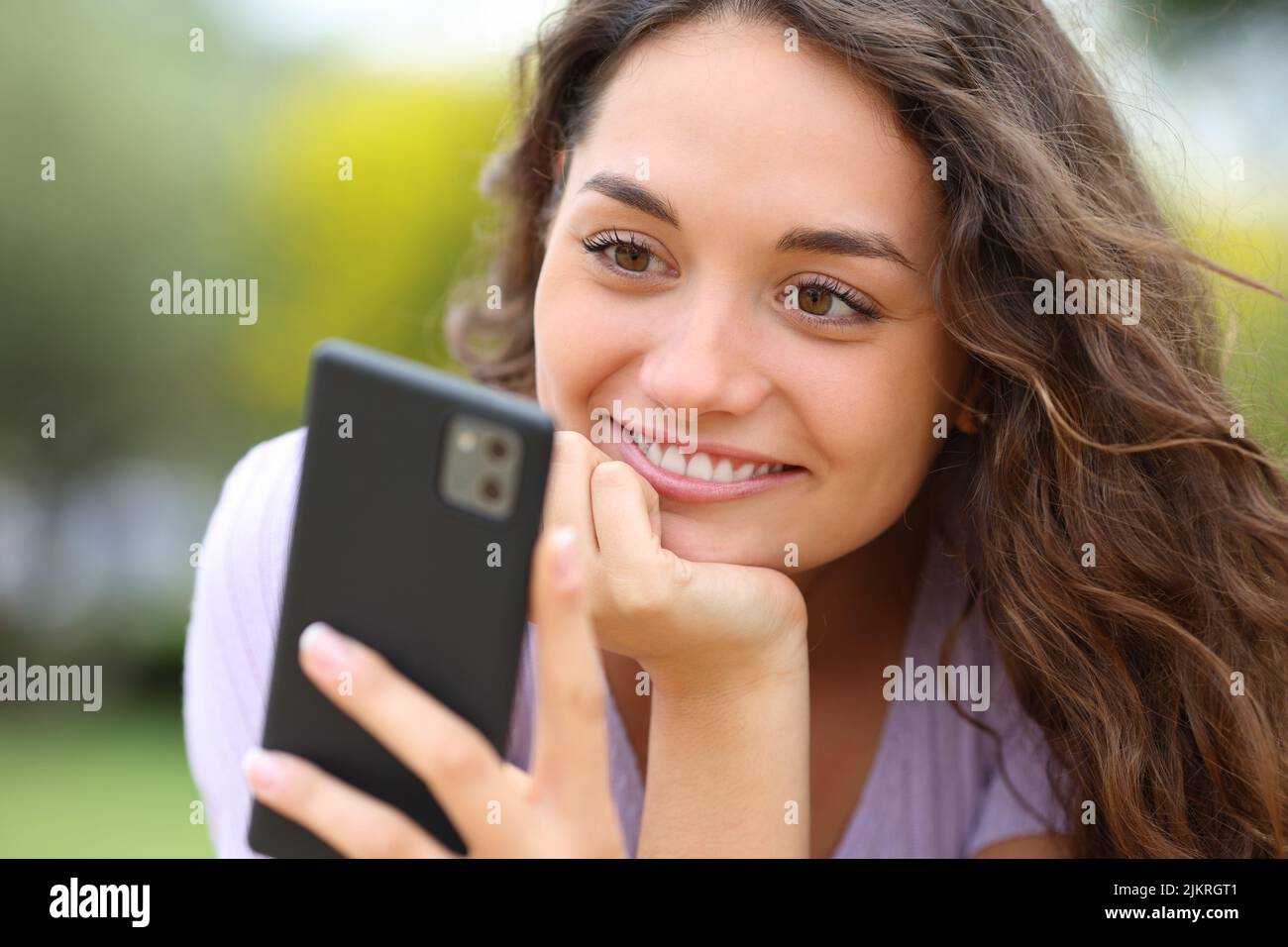 Donna felice di leggere il messaggio sul telefono cellulare in un parco Foto Stock