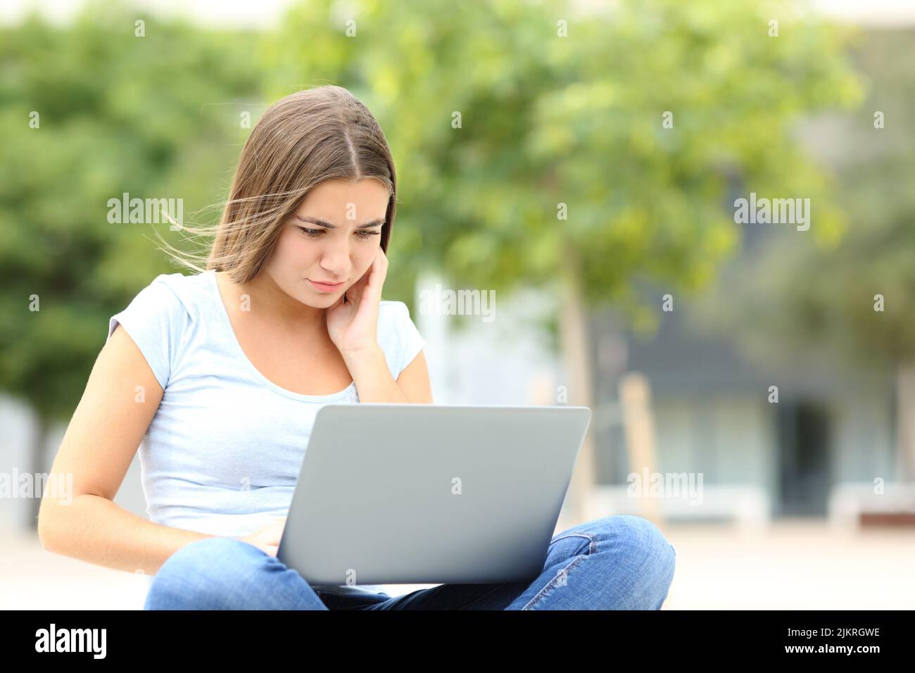 Teen concentrato utilizzando un computer portatile seduto in strada Foto Stock