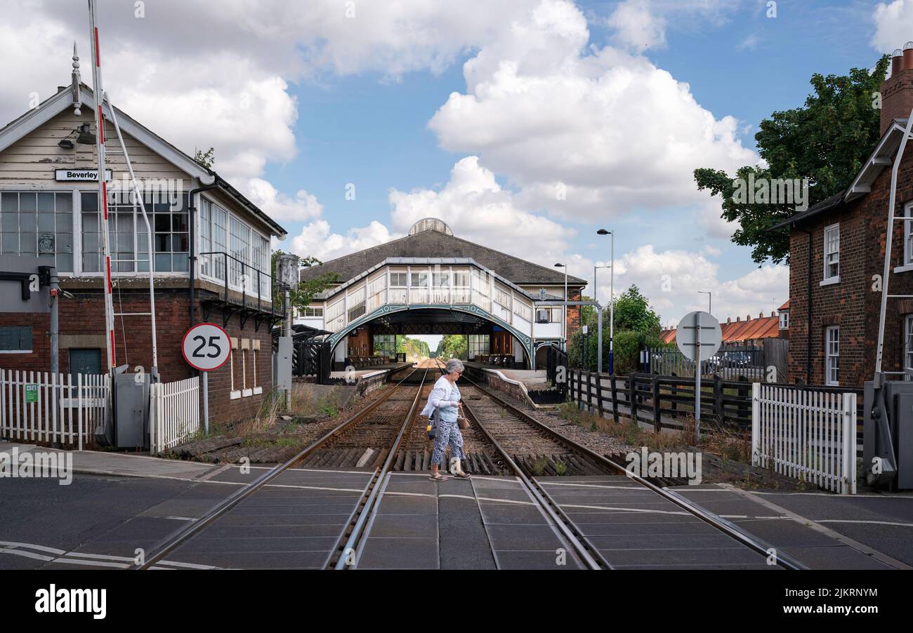 BEVERLEY, Regno Unito - 27 LUGLIO 2022: La donna attraversa le linee ferroviarie ai cancelli di swing e guarda la stazione ferroviaria in background a Beverley, Regno Unito. Foto Stock
